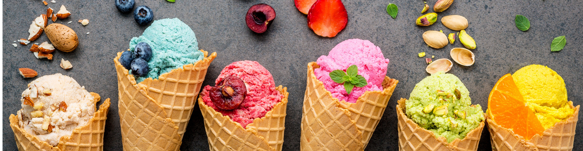 diverses sortes de glaces colorées sont alignées chacune dans une gaufrette Cornet sur une table : glace aux amandes, glace aux myrtilles, glace aux framboises, glace aux fraises, glace à la pistache, glace à l'orange.